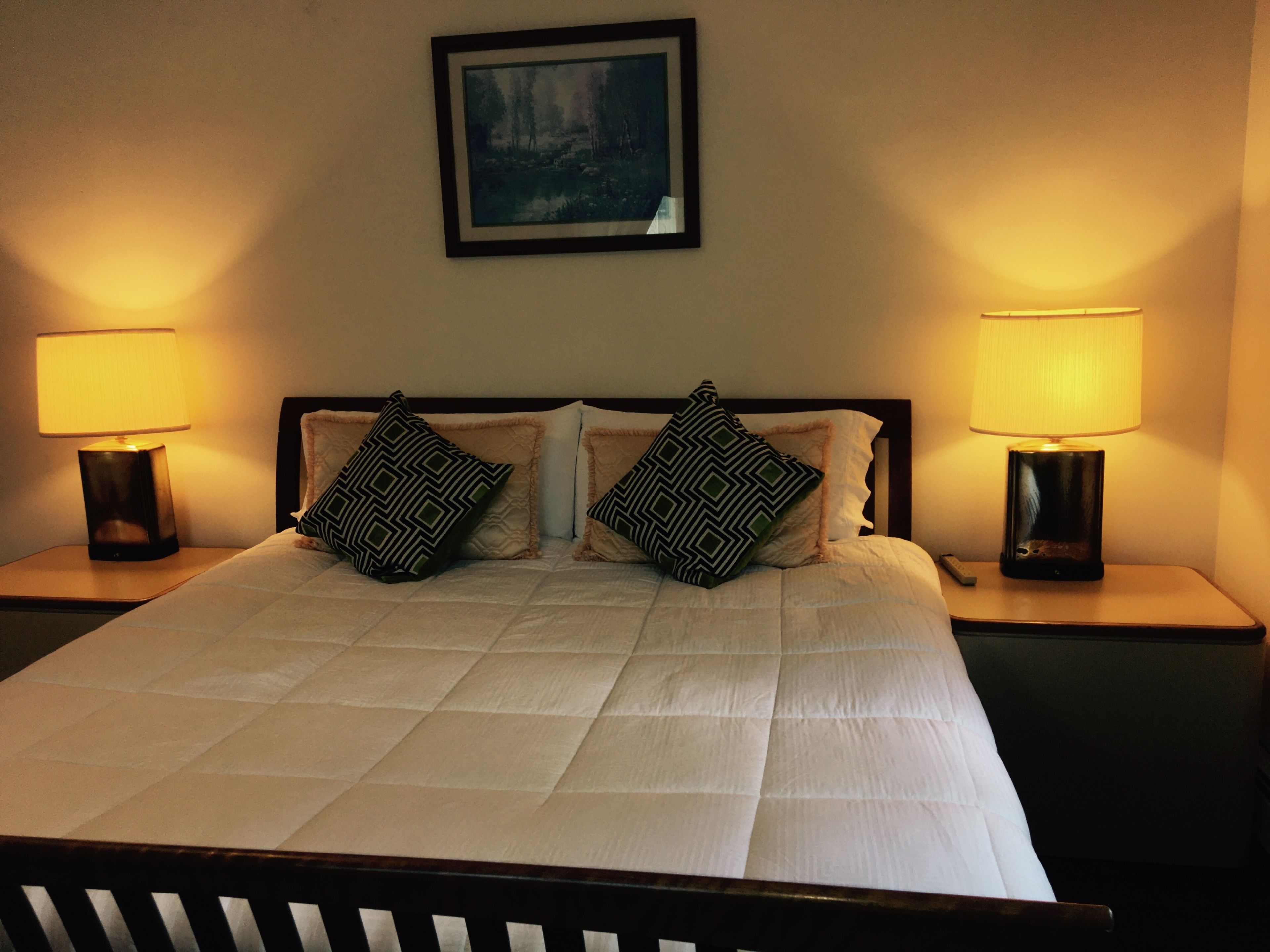 A neatly made bed with a white duvet, two patterned pillows, and two bedside lamps on either side.