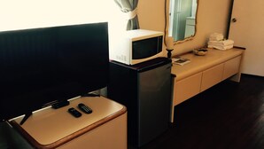 Una kitchenette compacta con microondas, refrigerador y una pequeña mesa con televisor y controles remotos.