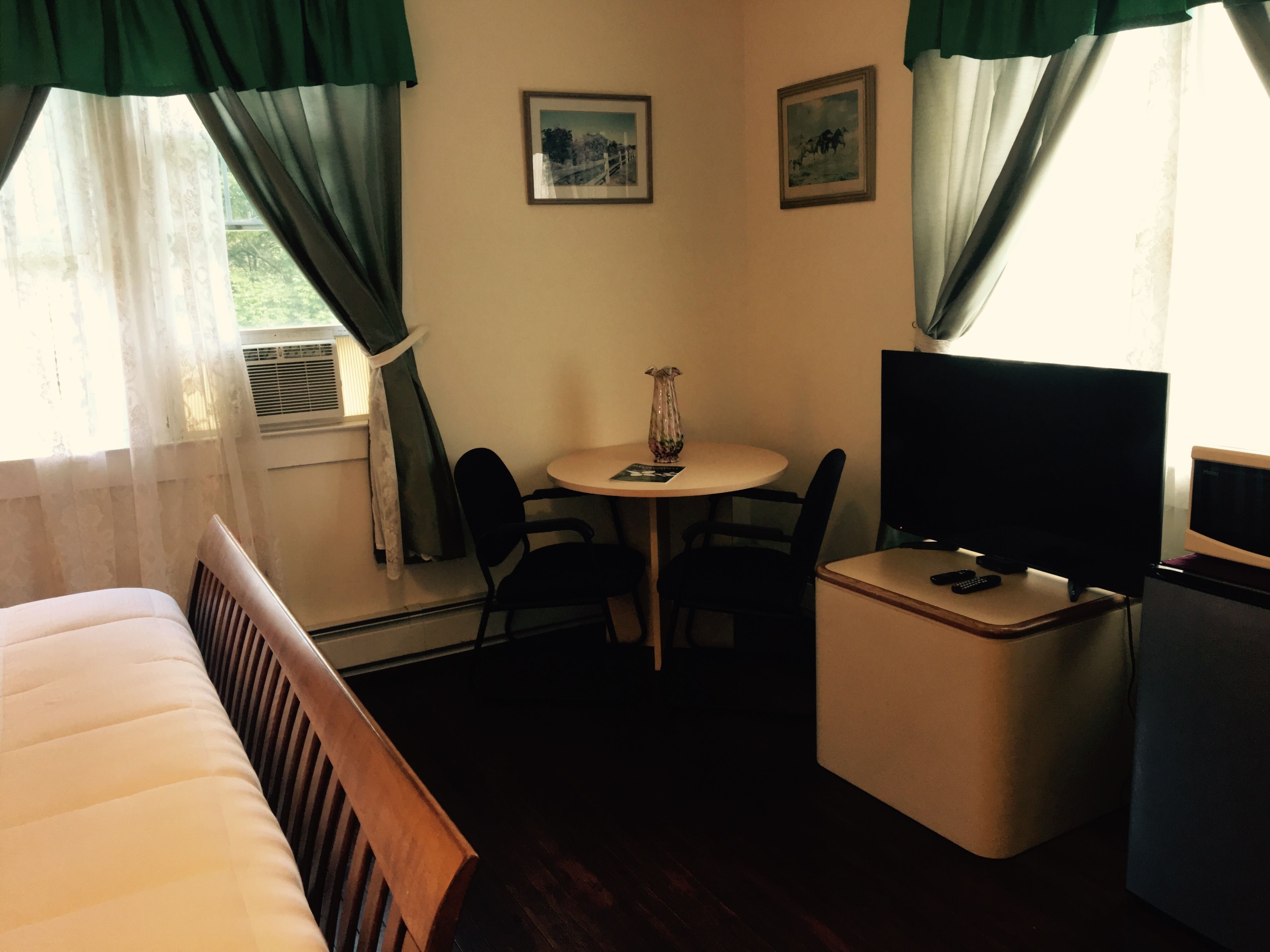 Een hotelkamer met een bed, een klein tafeltje met stoelen, een televisie en twee ingelijste foto's aan de muur.