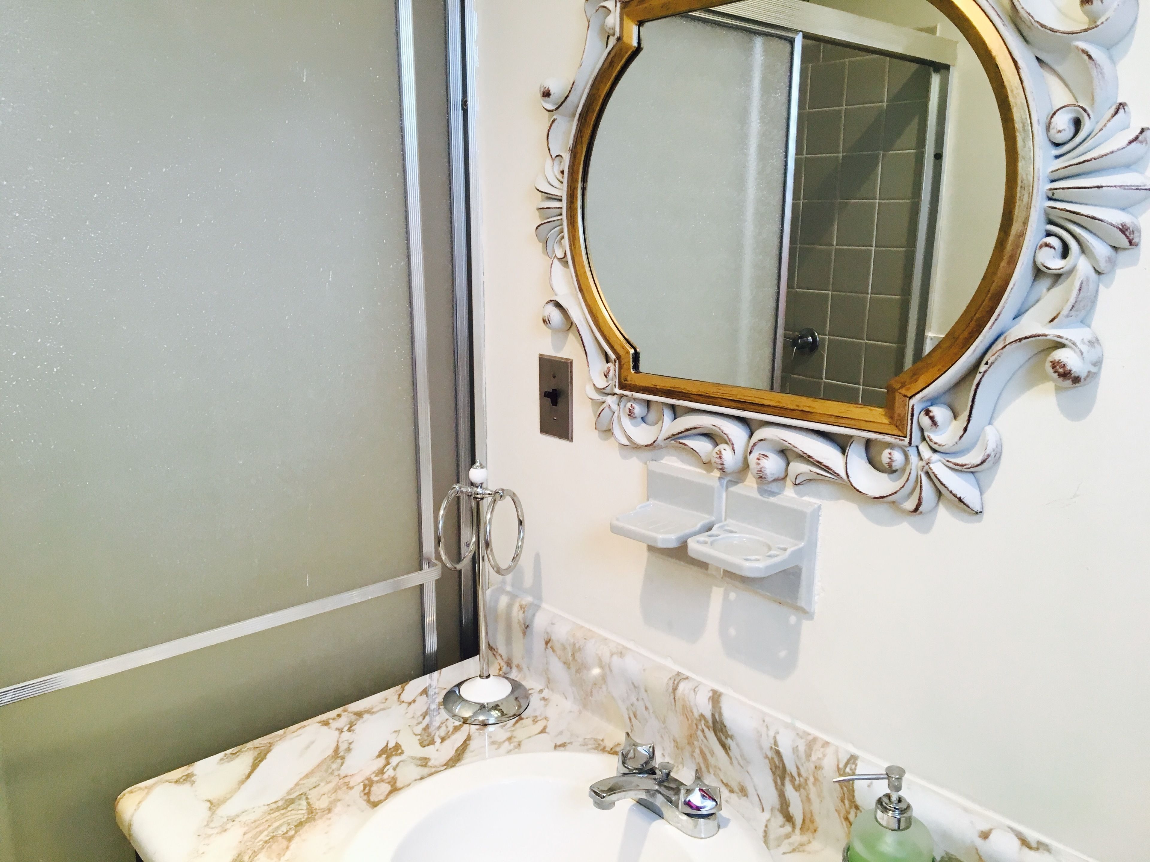 Une salle de bain avec un lavabo en marbre, un miroir encadré d’or et un espace douche.