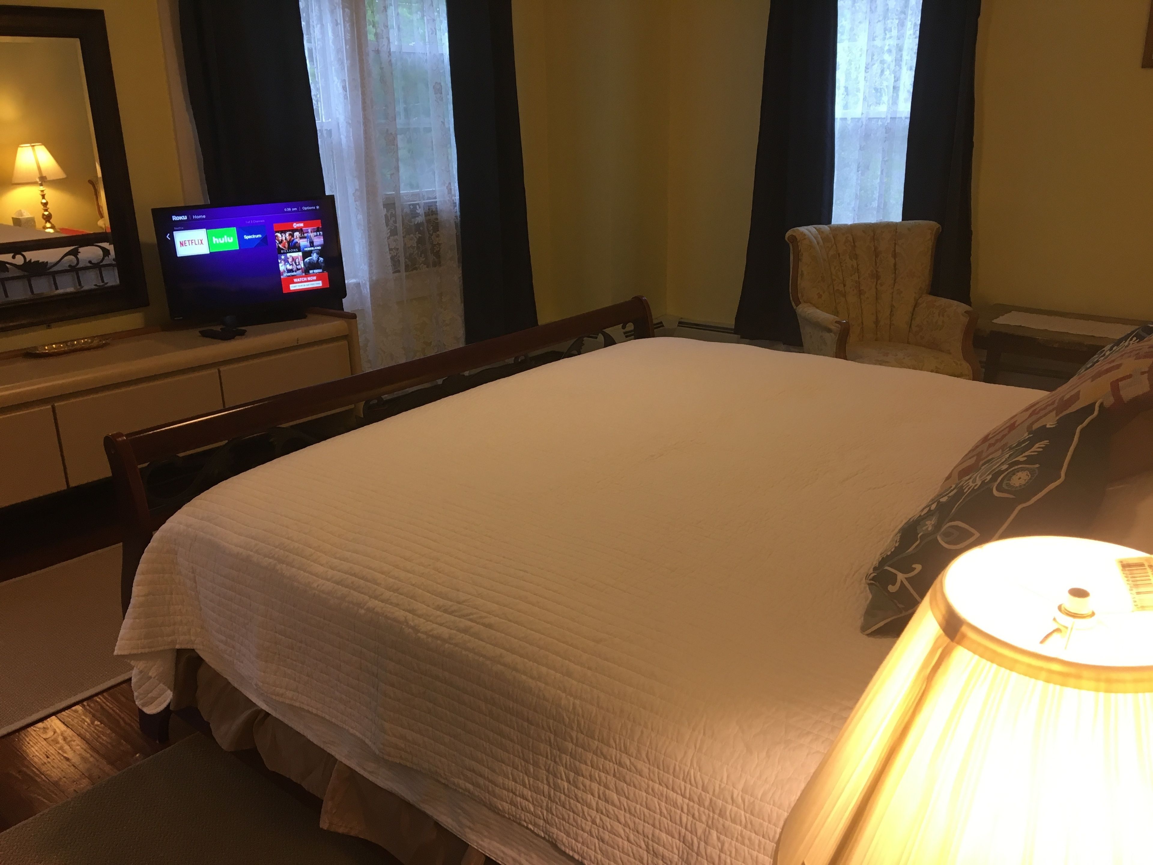Una habitación de hotel con una cama, un televisor en una cómoda, una silla y una lámpara.