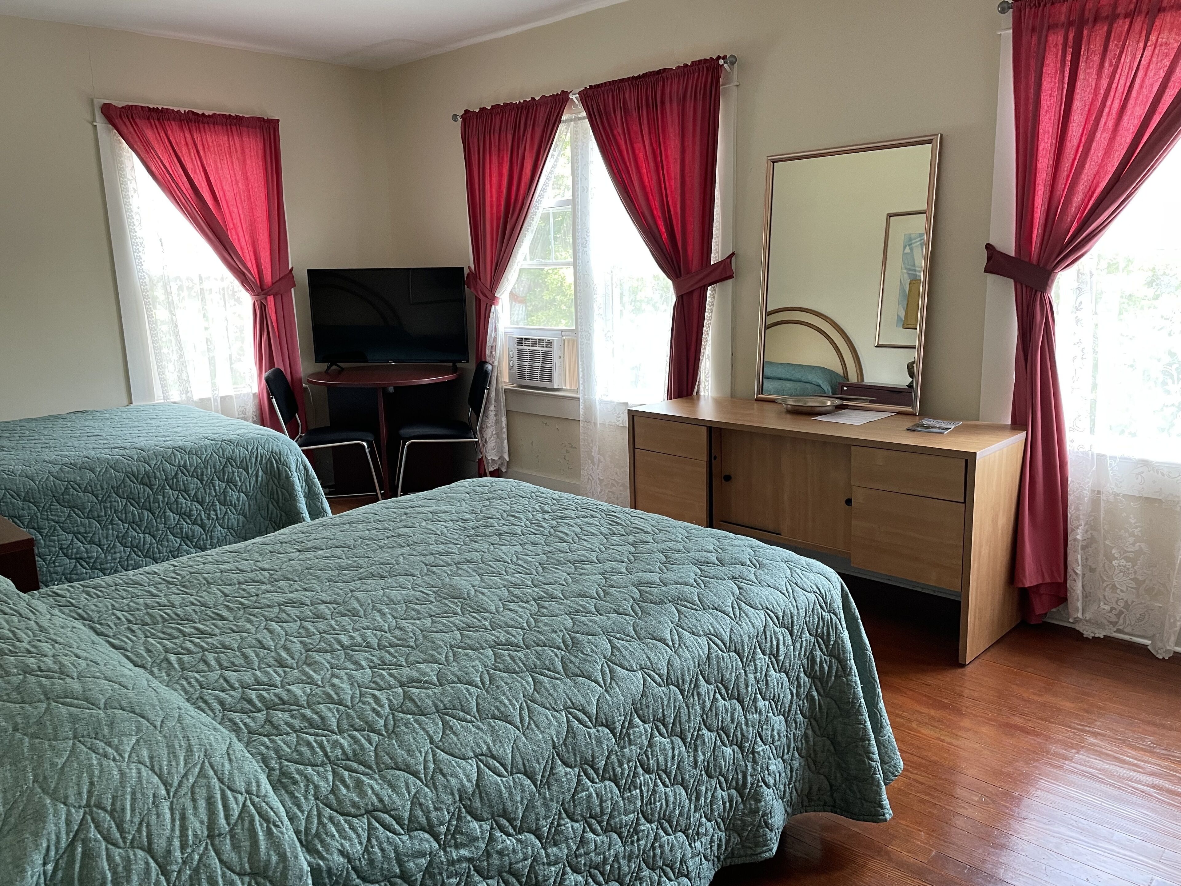 A hotel room with two beds, a TV, a desk, and a mirror.