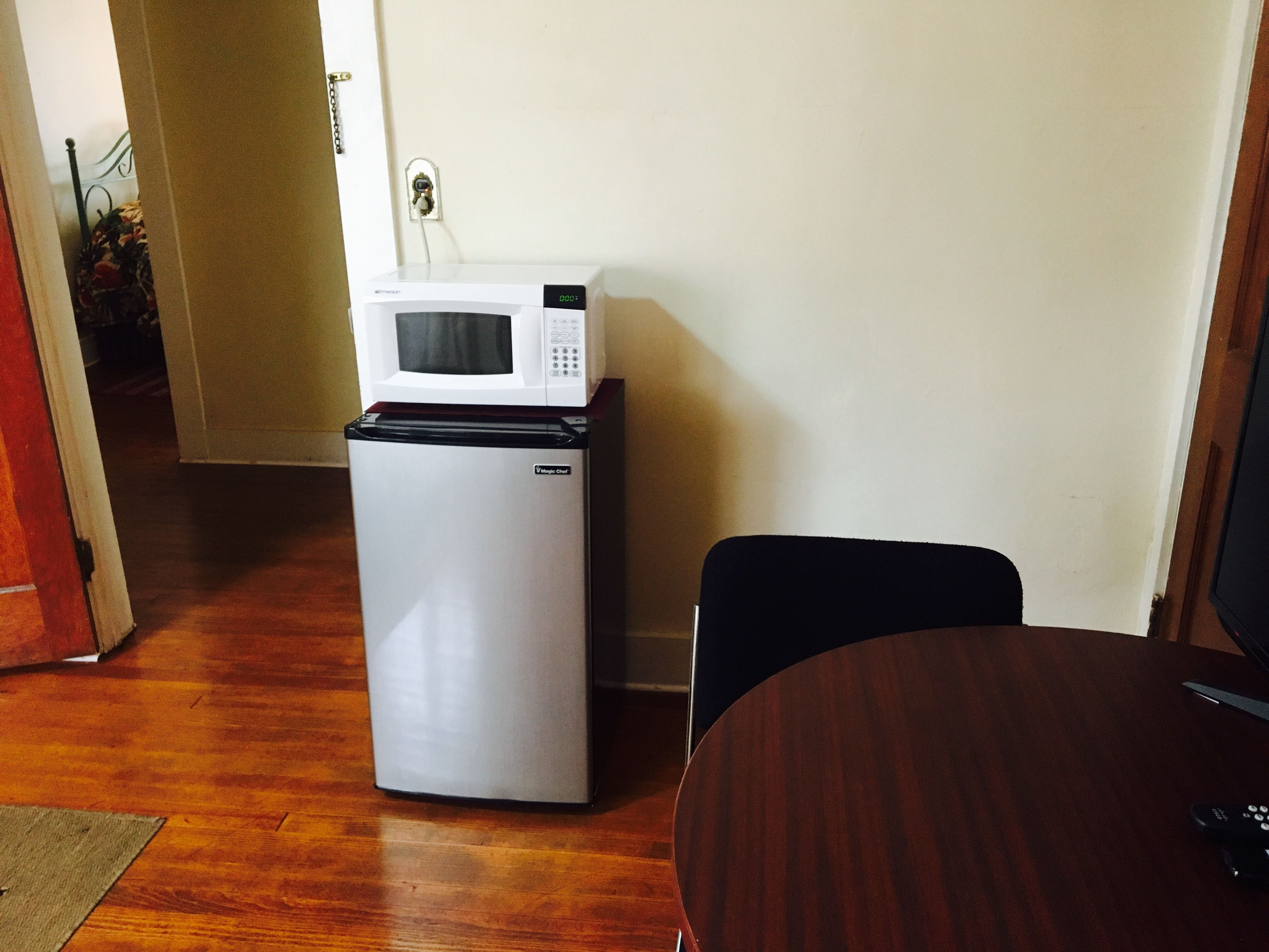 A compact kitchenette with a refrigerator, microwave, and a small table.