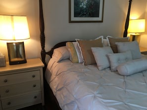 A neatly made bed with a white duvet and multiple pillows, flanked by two bedside tables with lamps, one of which has a tissue box on it.