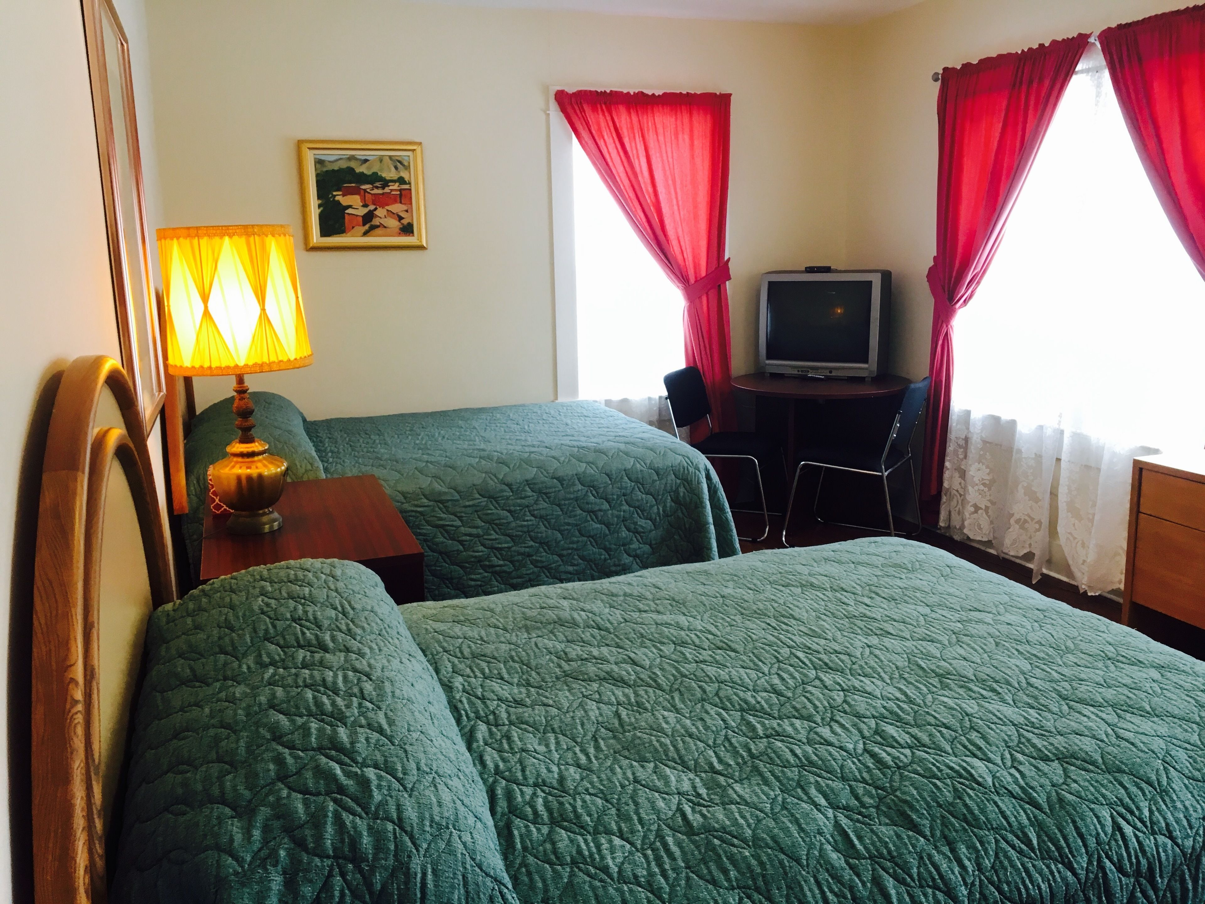 A hotel room with two beds, a desk with a television, a lamp, and a painting on the wall.
