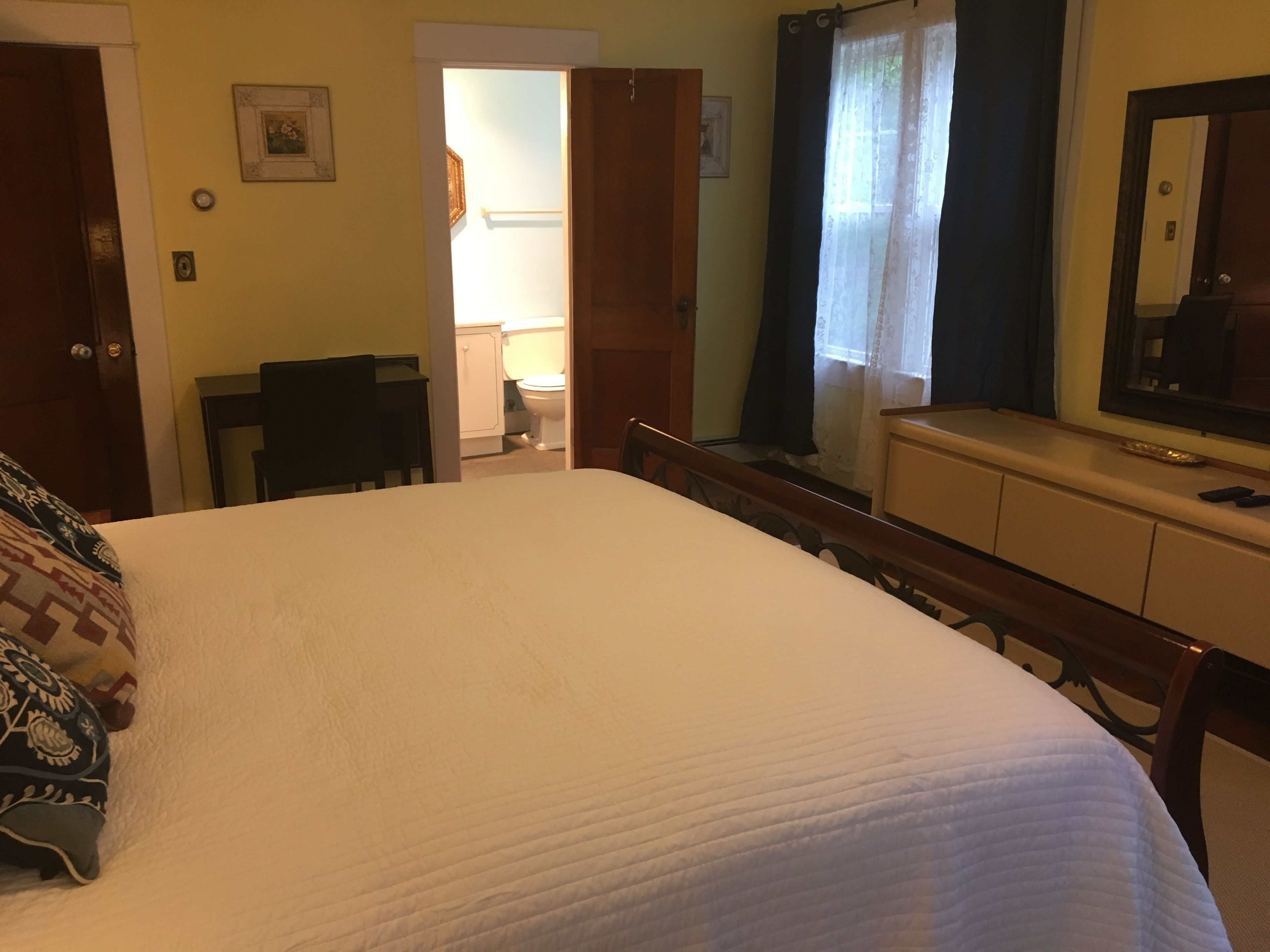 A bedroom with a bed, a dresser, a mirror, and a desk.