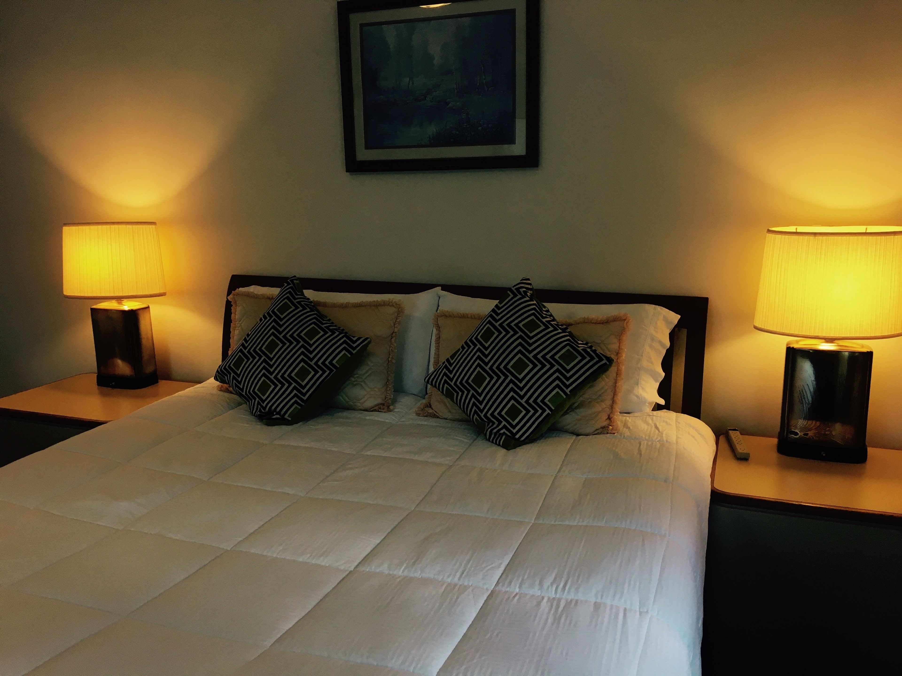 A neatly made bed with a white duvet, two black and white patterned pillows, and two bedside lamps on either side.