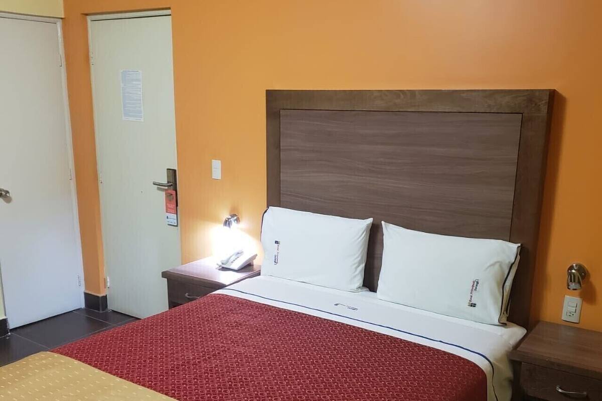 A hotel room with a large bed, a bedside table with a lamp, and a door with a sign.