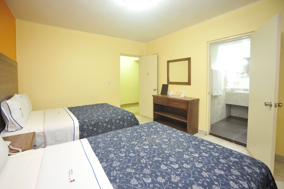 A hotel room with two beds, a wooden dresser, a mirror, and a bathroom door.