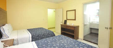 Habitación de hotel con dos camas, un aparador de madera, un espejo y la puerta del baño.