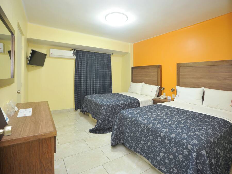 A hotel room with two beds, a desk, a mirror, and a television.
