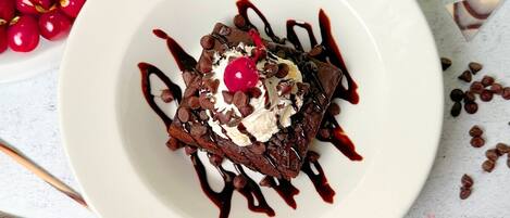 Dessert auf einem weißen Teller mit Kirschen, Schokoladenstückchen und Schlagsahne, gekrönt von einer Kirsche, umgeben von Schokoladenraspeln und einer Eisschale.