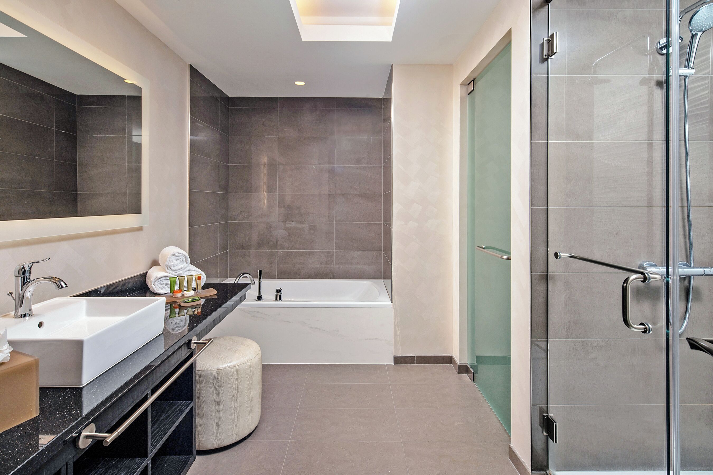 A modern bathroom with a large mirror, two sinks, a bathtub, and a walk-in shower.