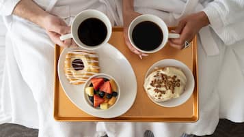 Una bandeja con dos tazas de café, un pastelito con glaseado blanco y un bol de fruta con fresas, arándanos y melón.