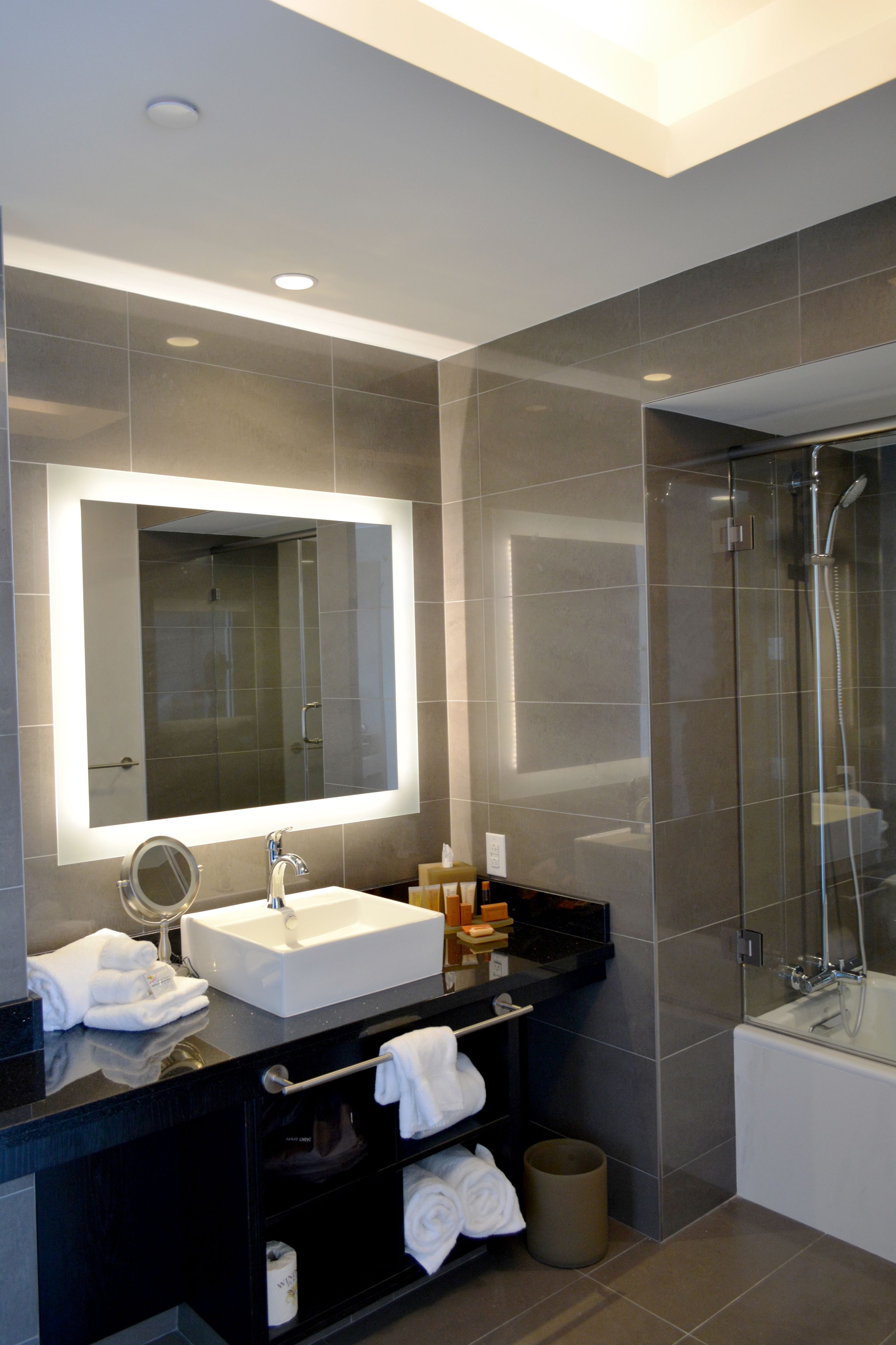 Une salle de bain moderne avec un grand miroir, un lavabo, une douche à parois de verre et un meuble-lavabo noir agrémenté de serviettes.