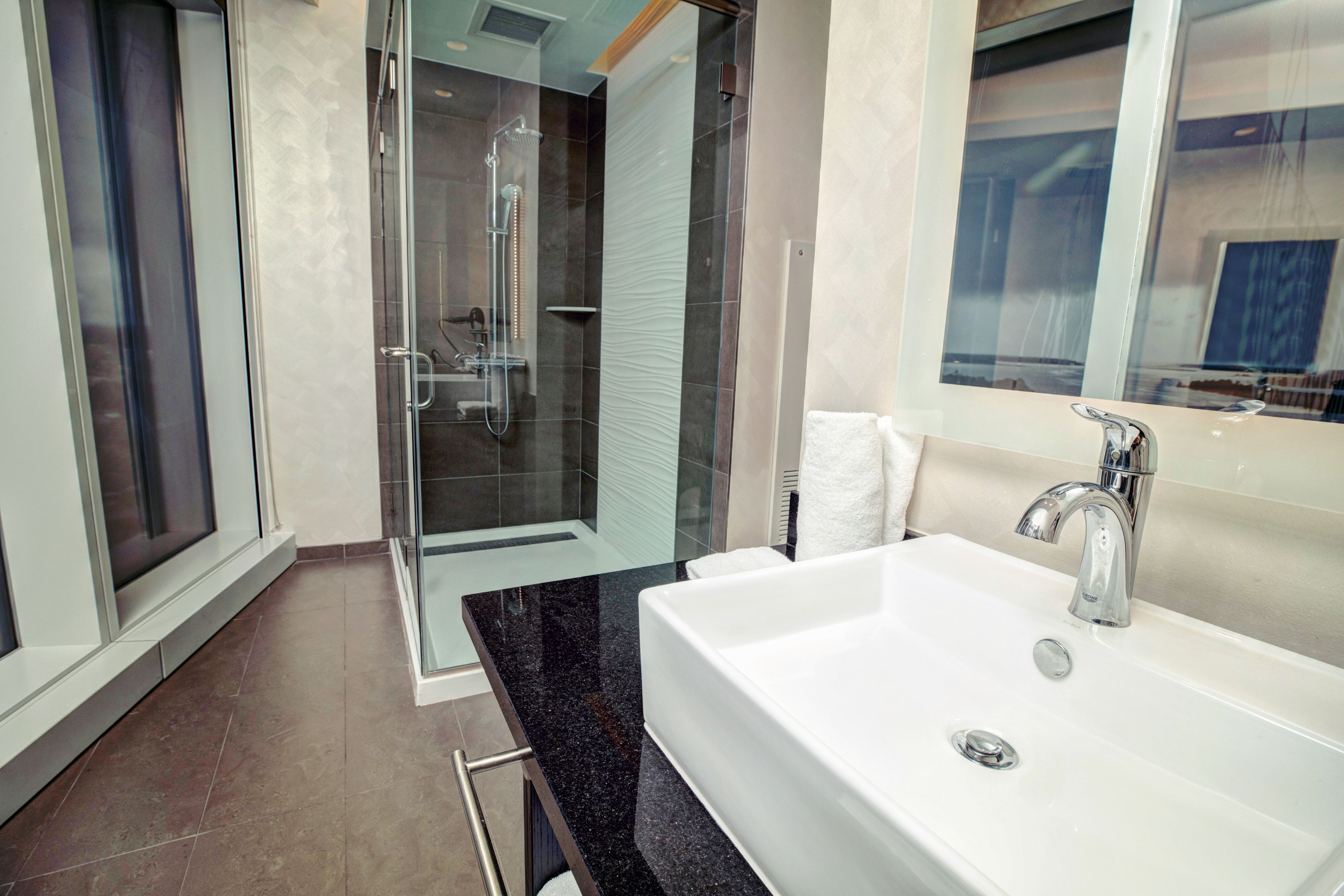 Ein modernes Badezimmer mit einem großen weißen Waschbecken, einer Glasdusche und einem großen Spiegel.