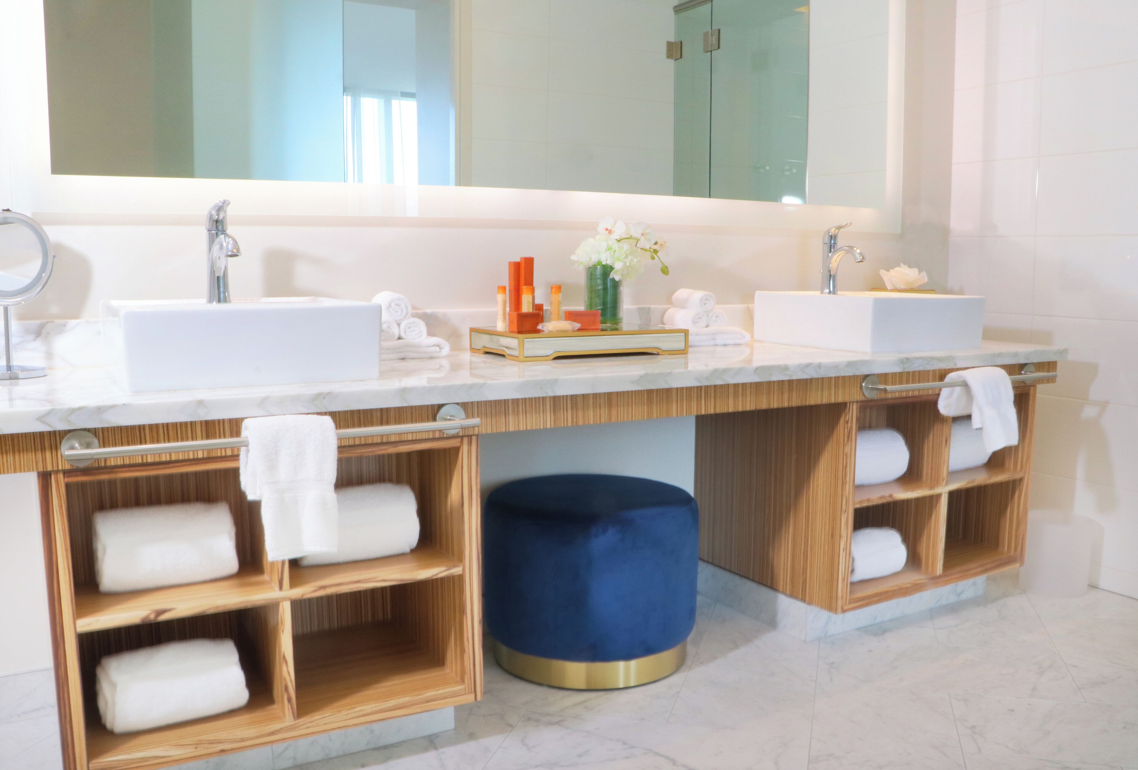 Une salle de bain moderne avec deux lavabos, un grand miroir et des étagères en bois où sont posées des serviettes.