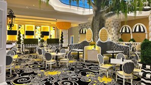 Un restaurant dont le sol est recouvert de motifs géométriques en noir et blanc, avec des chaises rayées de noir et de blanc, et un grand arbre décoré de guirlandes lumineuses.