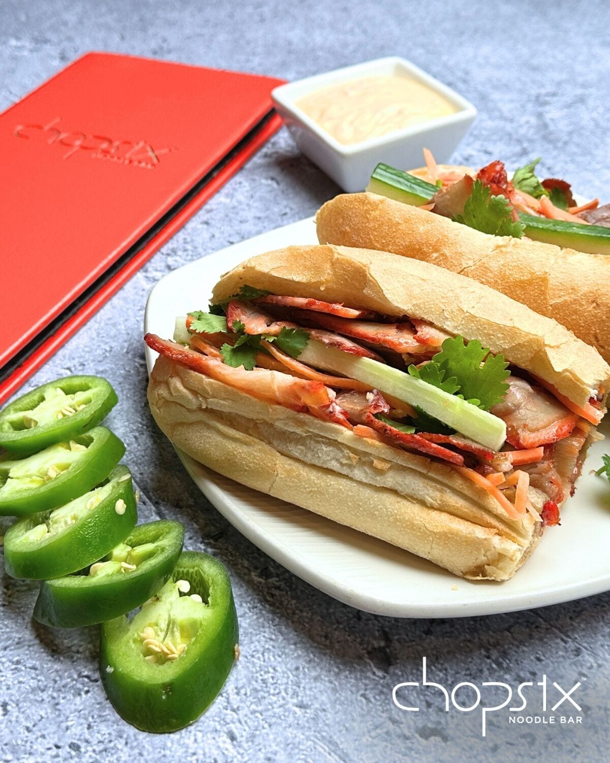 Ein Sandwich mit verschiedenen Zutaten, ein Teller und eine kleine Schüssel Soße.