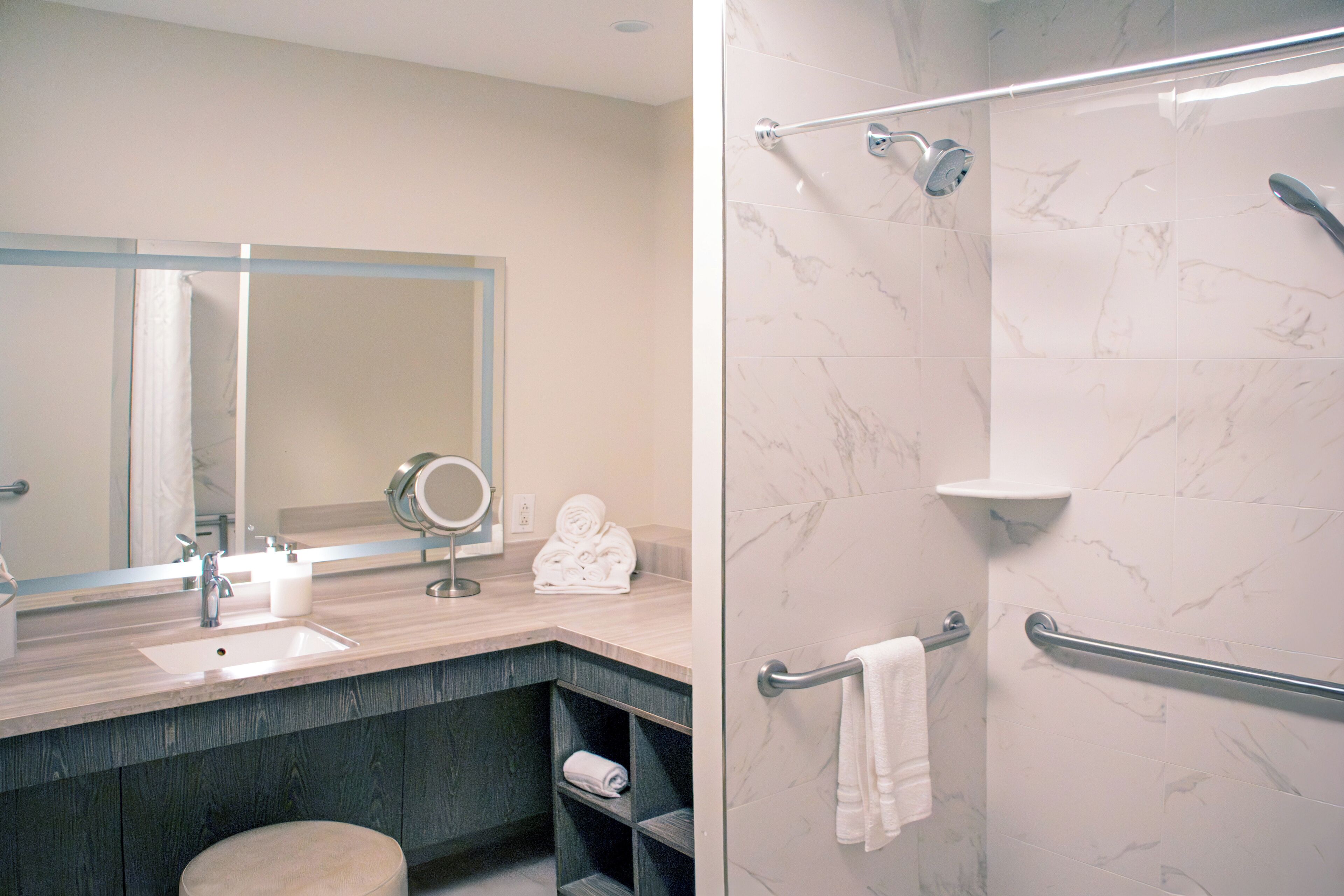 A modern bathroom with a sink, mirror, towel rack, and shower area.