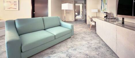 A hotel room with a light green sofa, a flat-screen TV, a minibar, and a marble-patterned carpet.