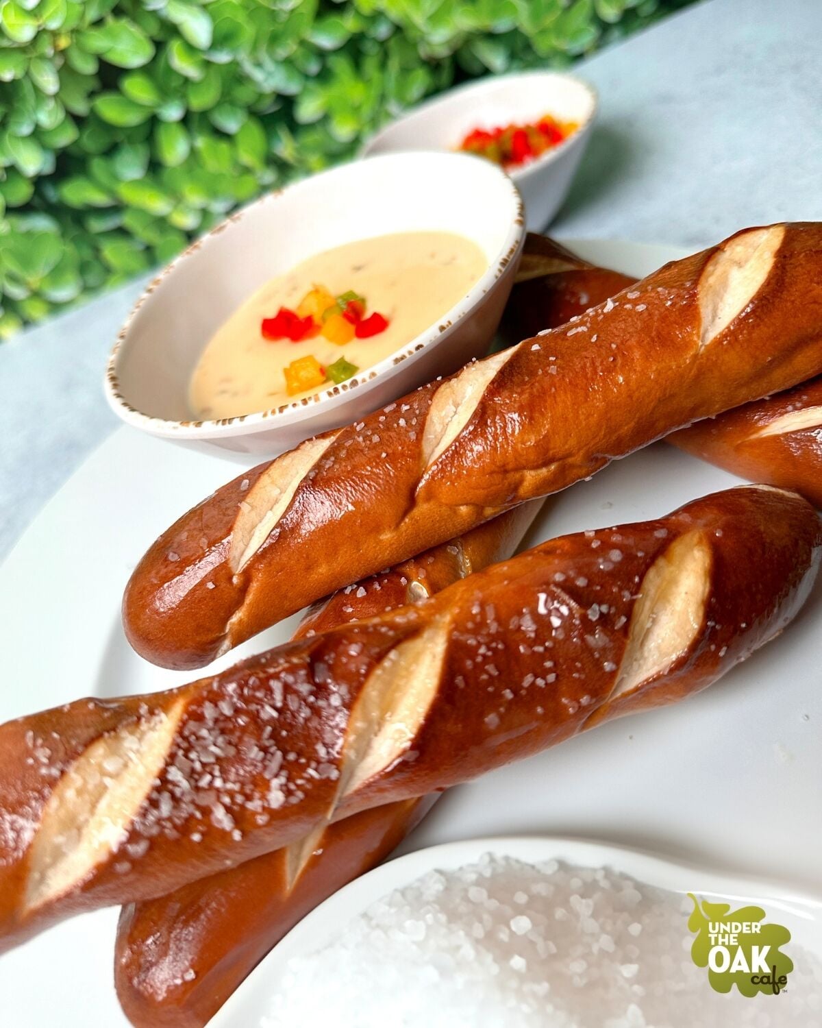 Three baguettes with salt on a white plate, accompanied by two bowls of dipping sauces.