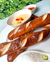 Three baguettes with salt on a white plate, accompanied by two bowls of dipping sauces.