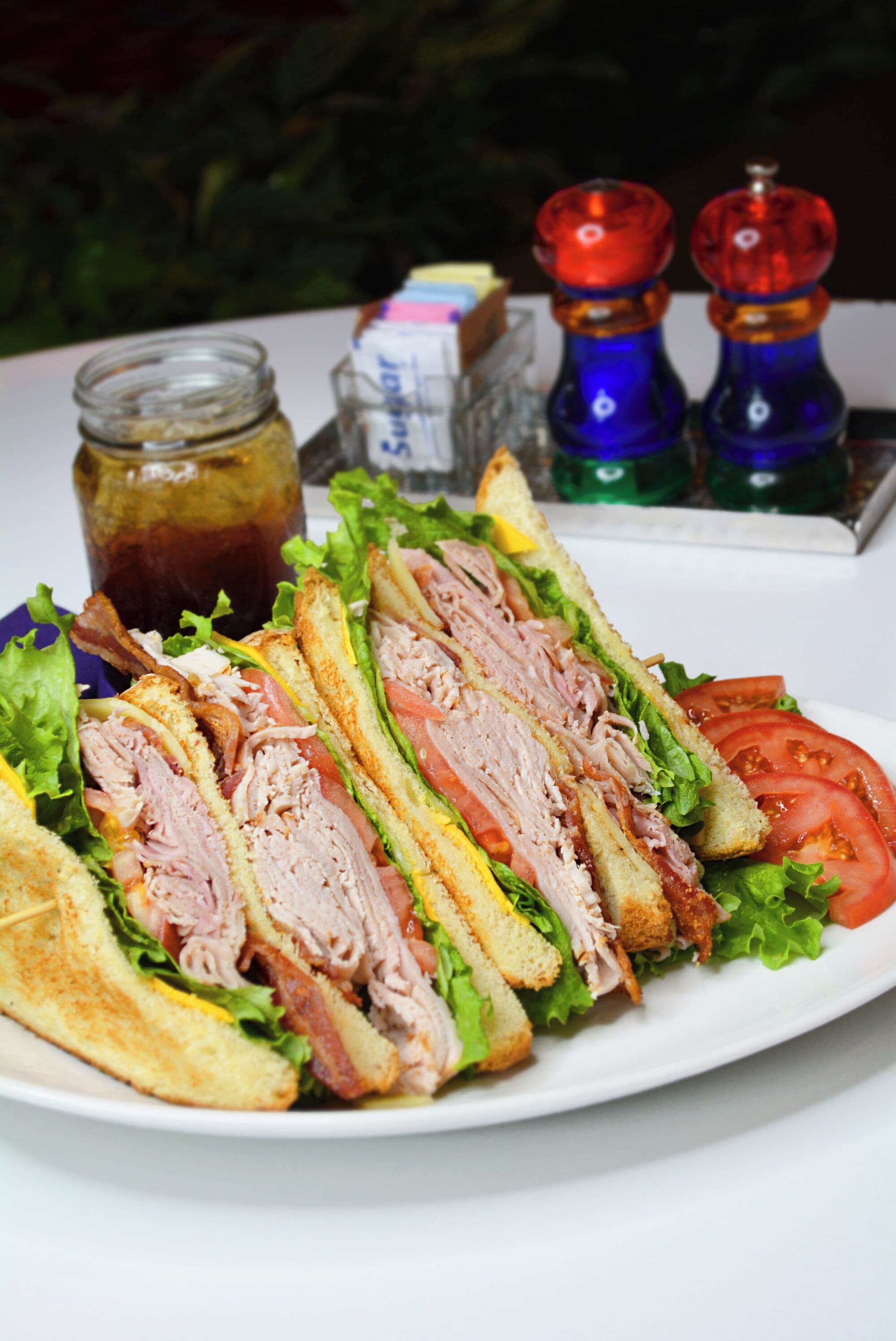 A sandwich with lettuce, tomato, and meat on a white plate.