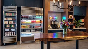 A modern café with a wooden table, a coffee station, and refrigerated beverage dispensers.