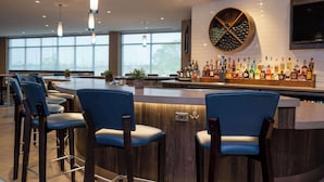A modern bar area with a wooden bar counter, blue bar stools, and a wine rack.