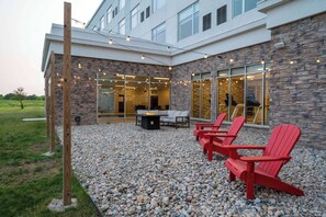 Un bâtiment moderne avec une façade en pierre, un espace extérieur aménagé avec des fauteuils Adirondack rouges et un foyer.