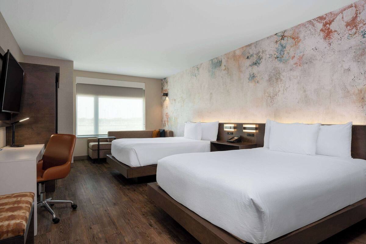Une chambre d’hôtel avec deux lits, un bureau, une chaise et un téléviseur.