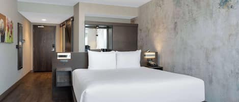 Una habitación de hotel moderna con una cama grande, piso de madera, pared de acento de concreto y un espejo sobre la cama.