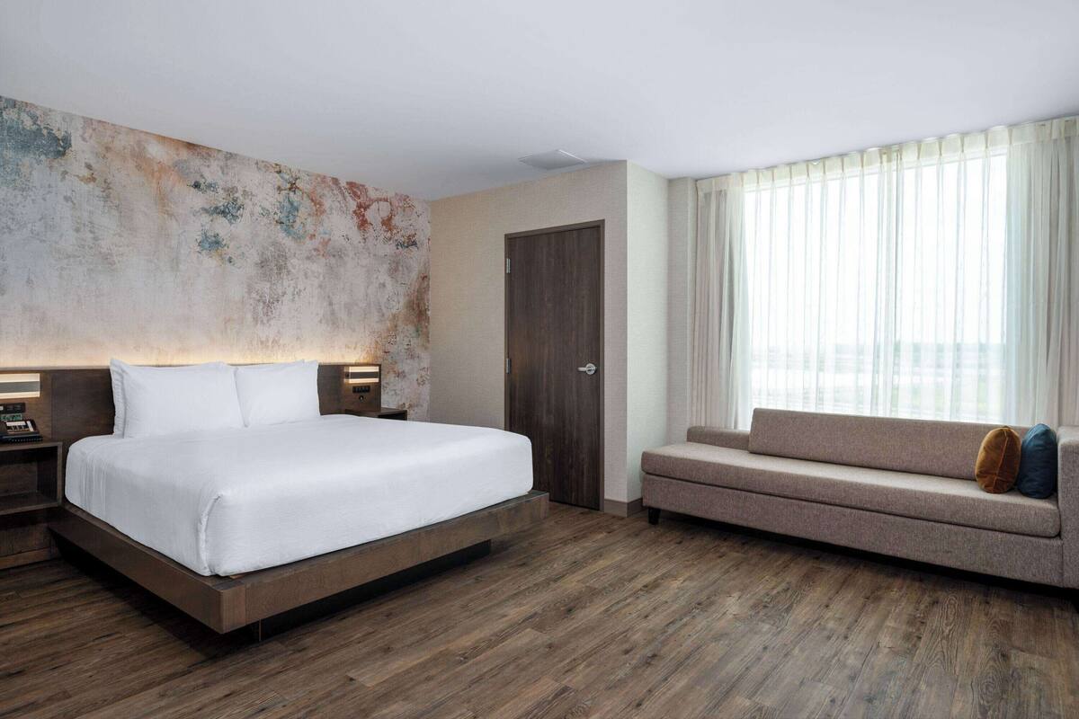 Une chambre d’hôtel avec un grand lit, un canapé, un plancher en bois, une porte et une fenêtre avec des rideaux.