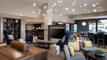 A modern hotel lobby with leather sofas, a flat-screen TV, a fireplace, and a bar area.