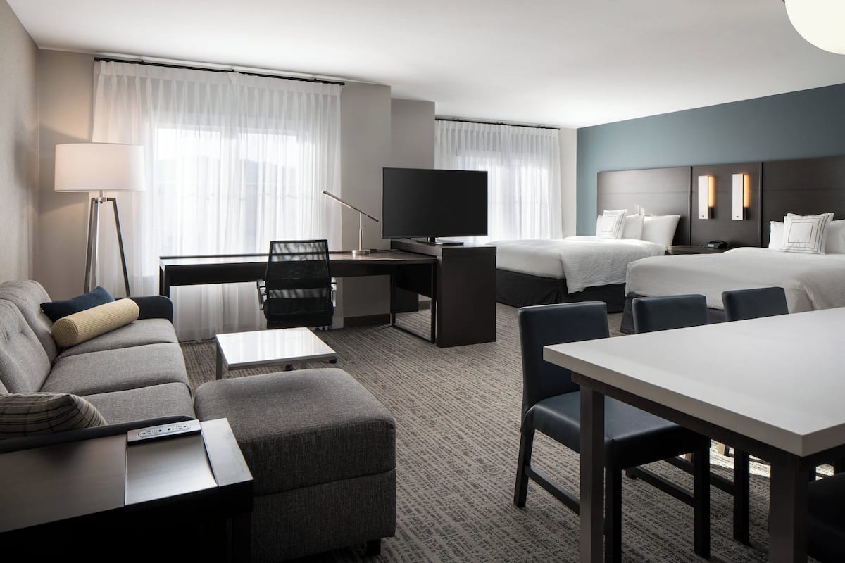 A hotel room with a sofa, a desk with a TV, a bed, and a dining table.