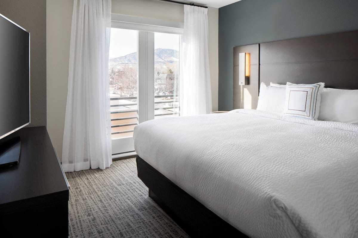 A hotel room with a large bed, a television on a stand, and a view of the outdoors through a window.