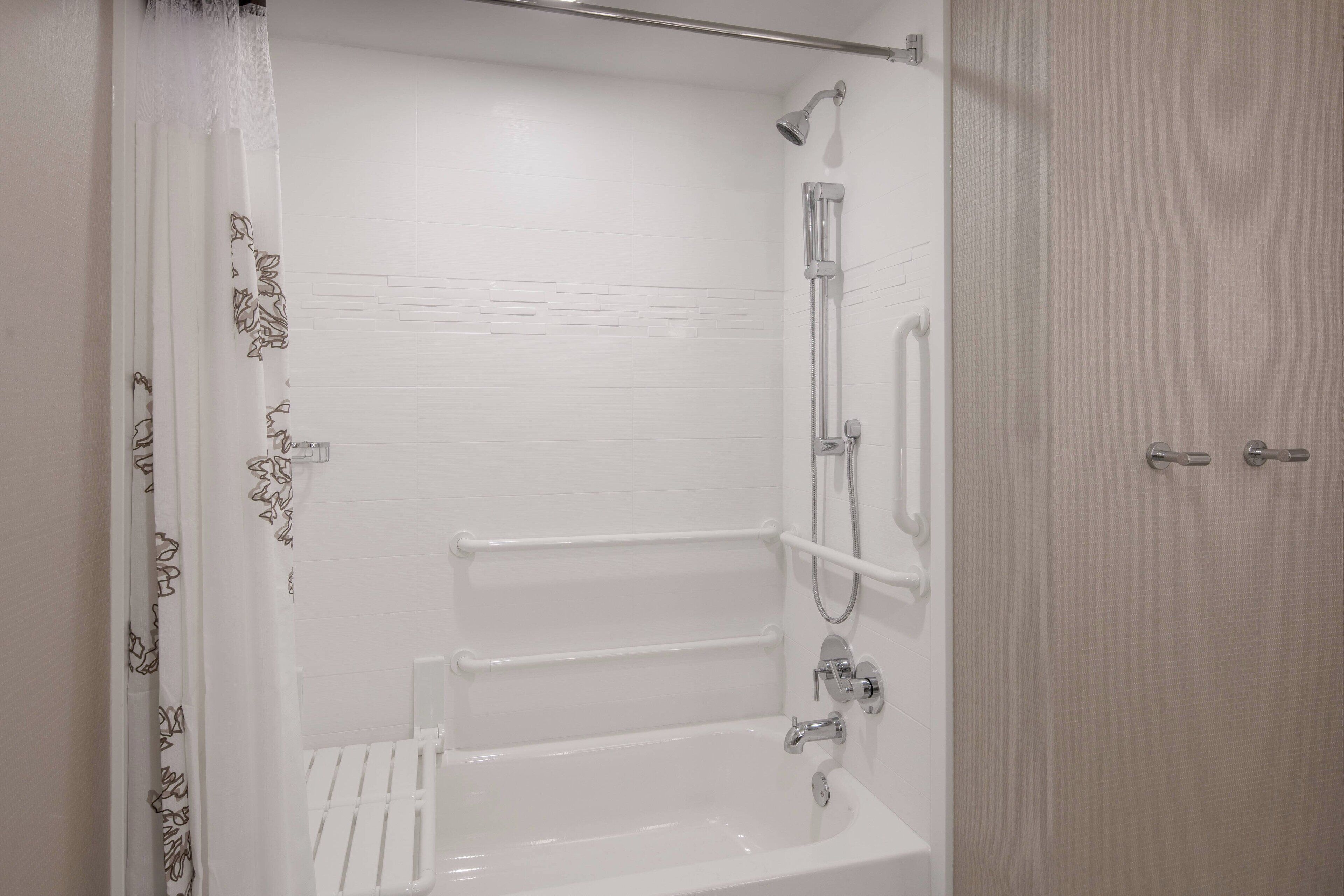A modern bathroom with a bathtub, shower, and handrails.