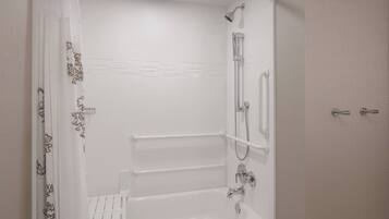 A modern bathroom with a bathtub, shower, and handrails.