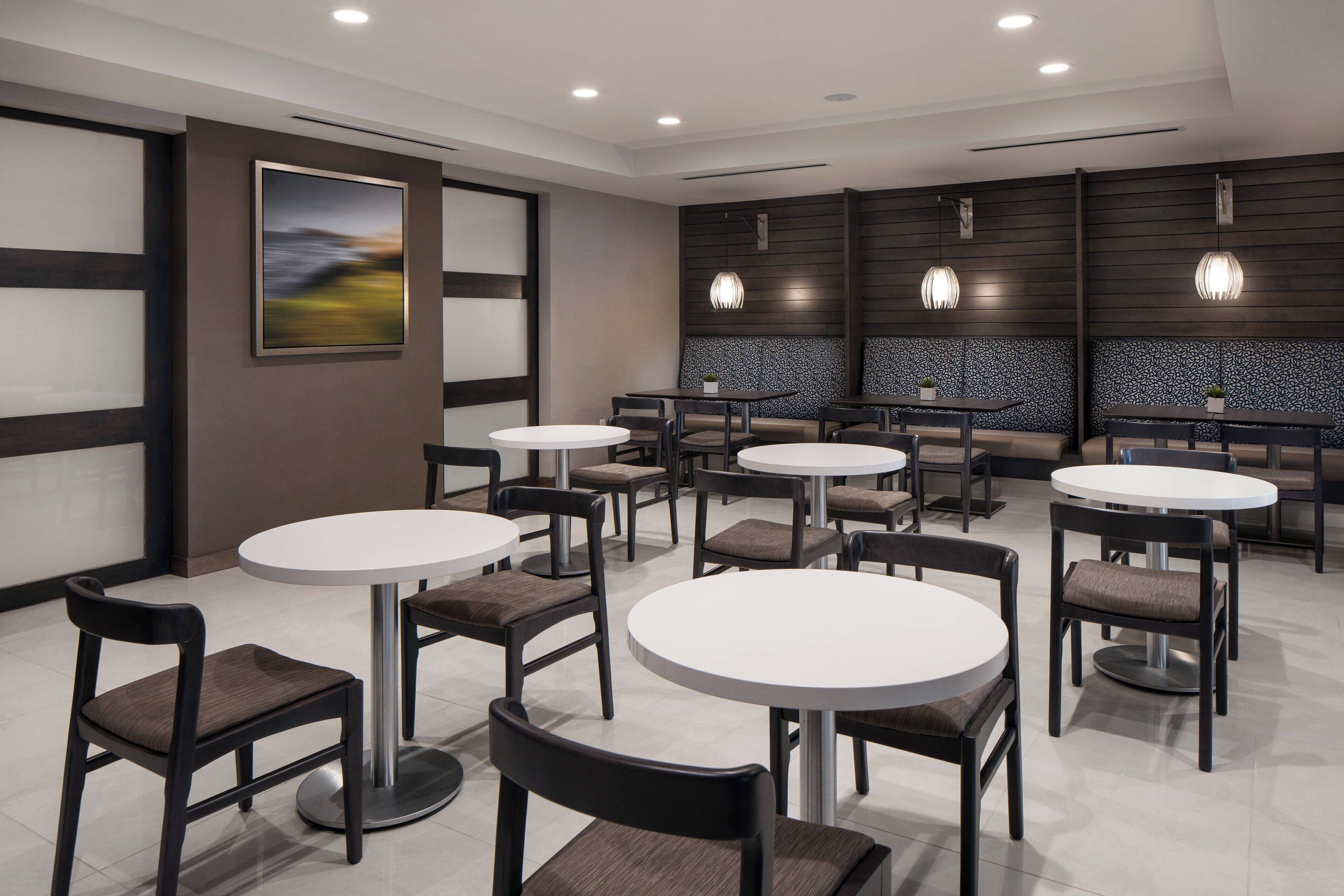 Um restaurante moderno com mesas e cadeiras redondas, um quadro grande na parede e iluminação pendente.
