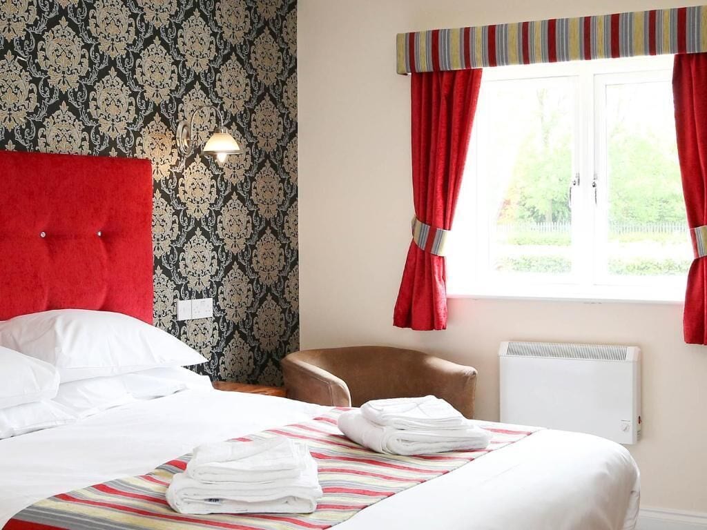 Une chambre d’hôtel avec un lit, une chaise, une fenêtre avec des rideaux et un radiateur.