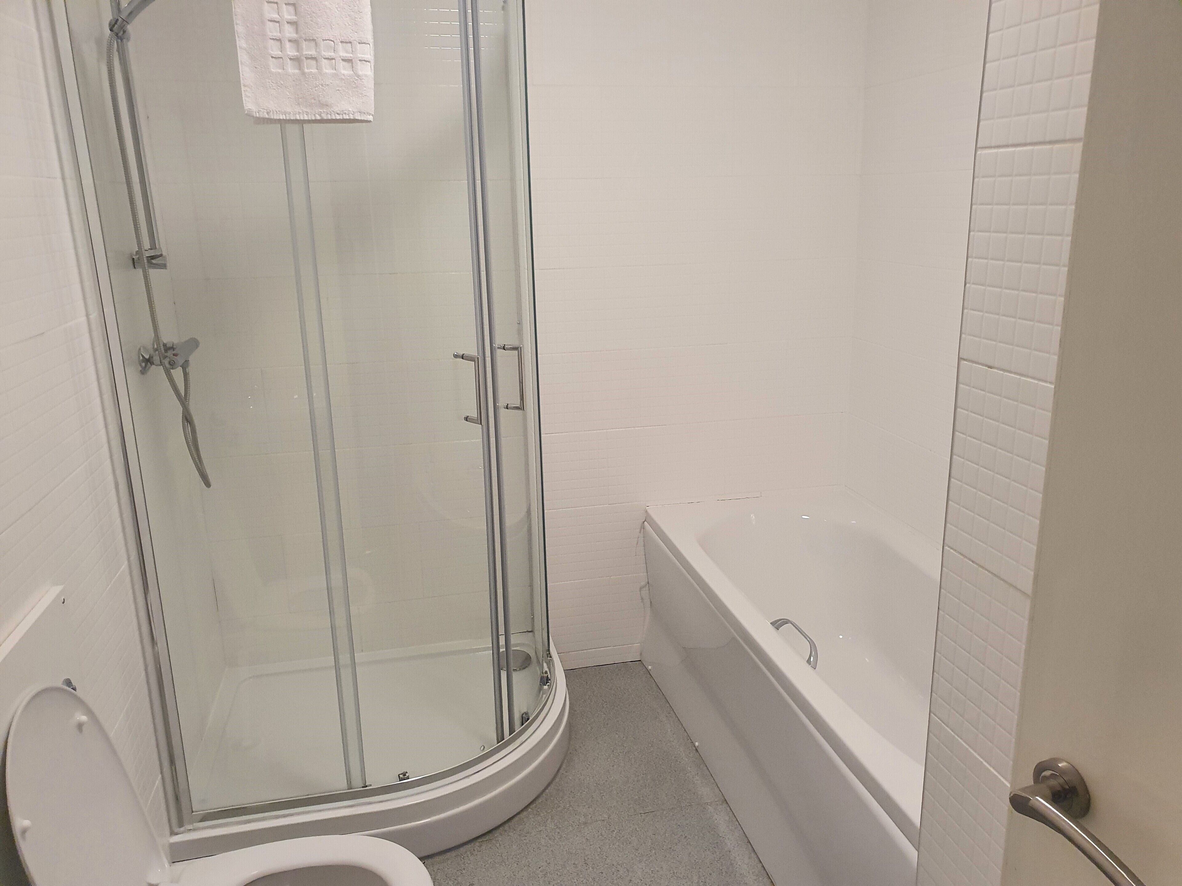 A bathroom with a glass-enclosed shower, a white bathtub, and a toilet.