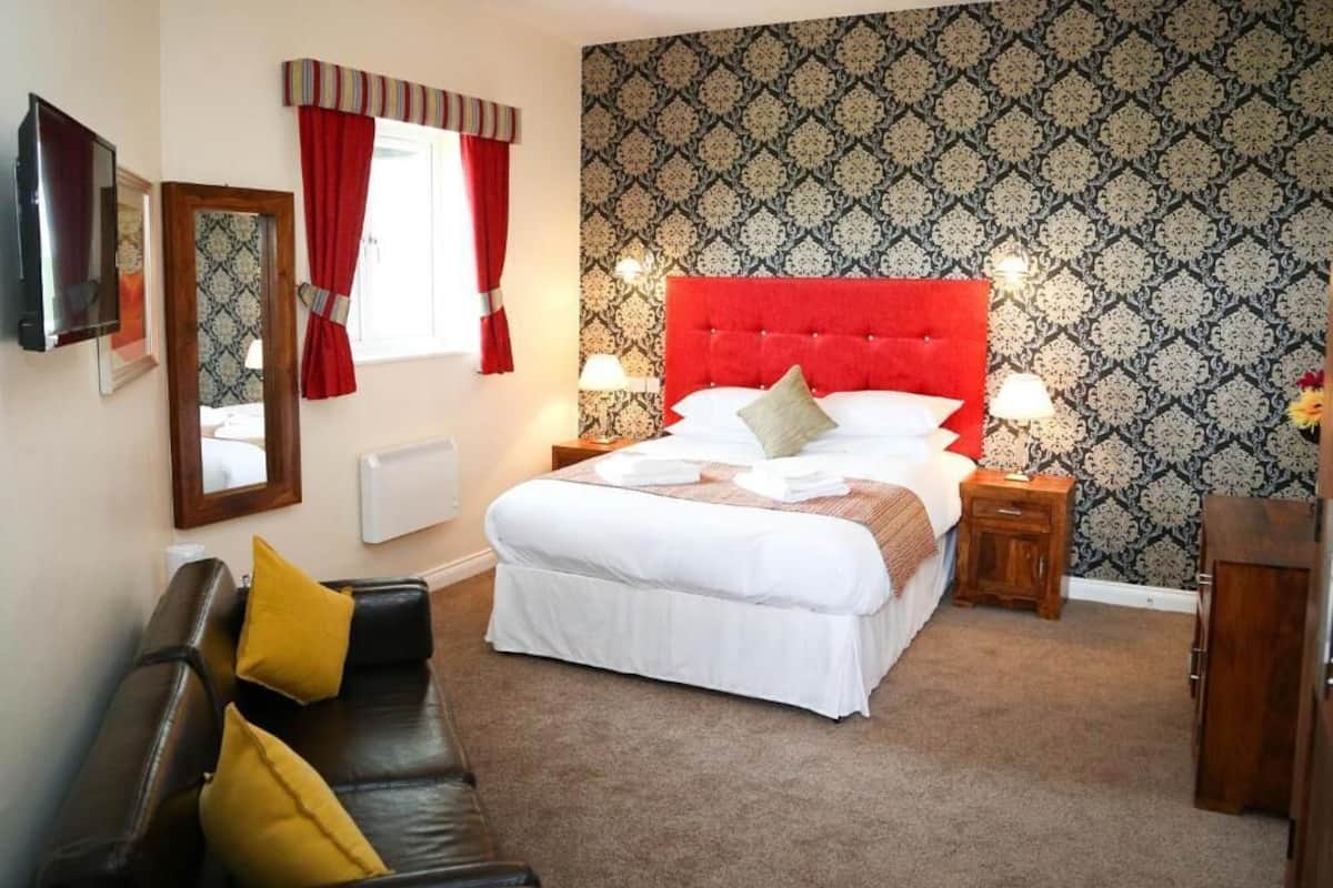 Une chambre à coucher avec un grand lit, une table de chevet en bois, un canapé en cuir noir et un miroir au mur.