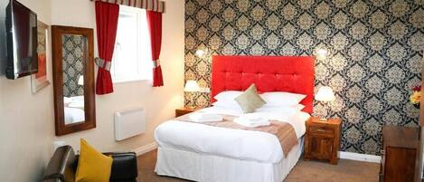 A bedroom with a large bed, a wooden nightstand, a black leather sofa, and a mirror on the wall.