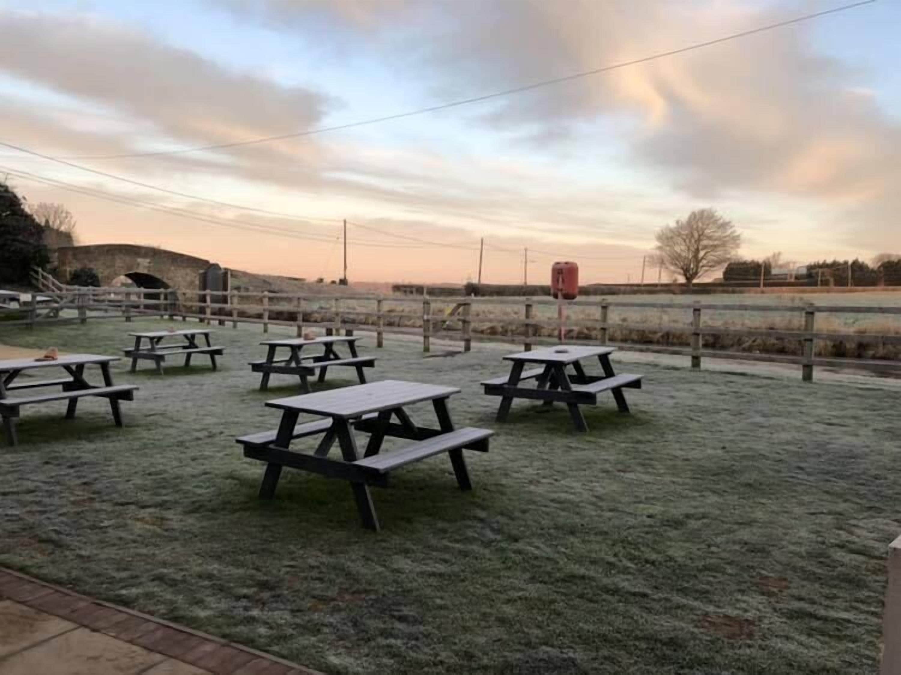 An outdoor picnic area with multiple wooden picnic tables and a fence.
