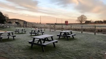 An outdoor picnic area with multiple wooden picnic tables and a fence.