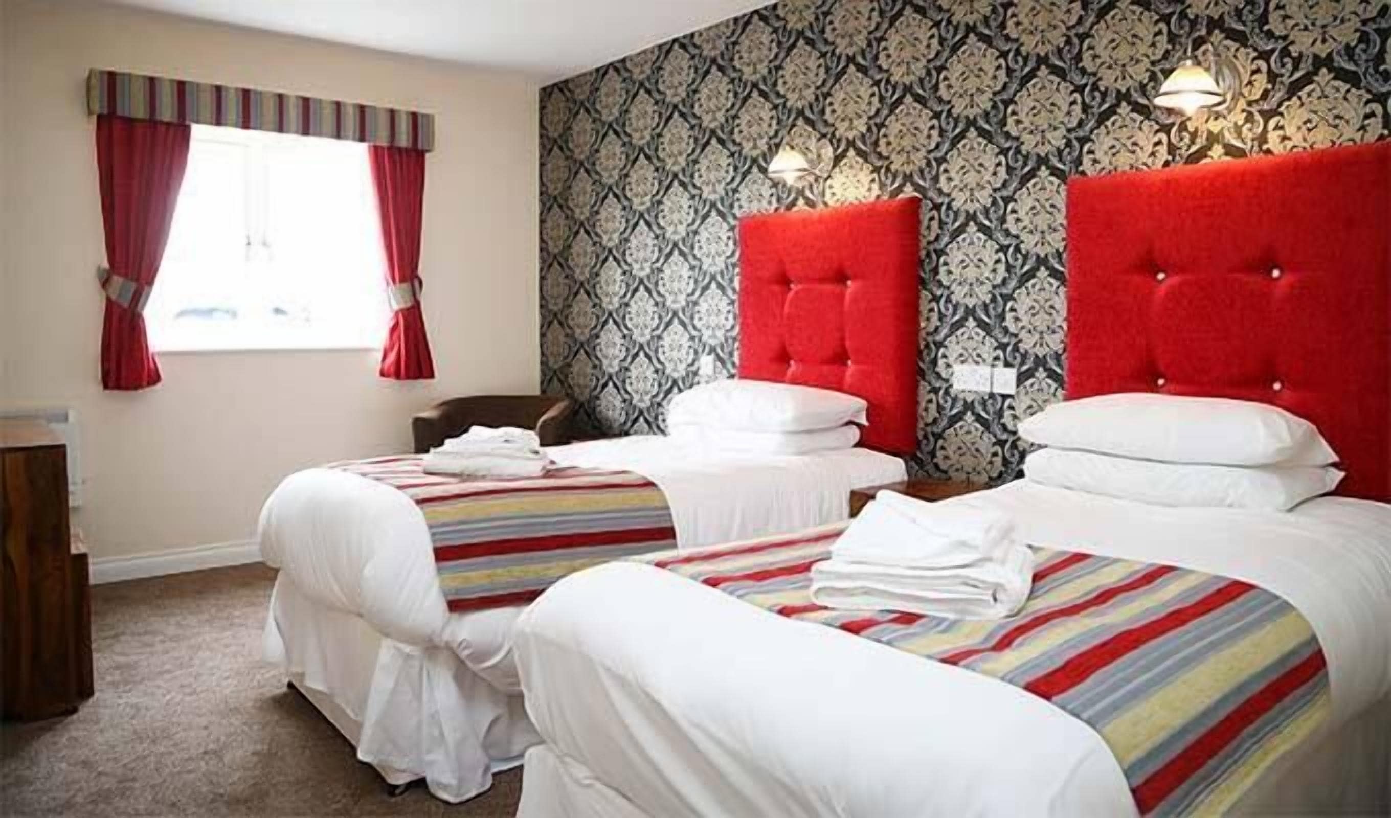 Une chambre d’hôtel avec deux lits, une literie à rayures, une tête de lit rouge et un papier peint à motifs.