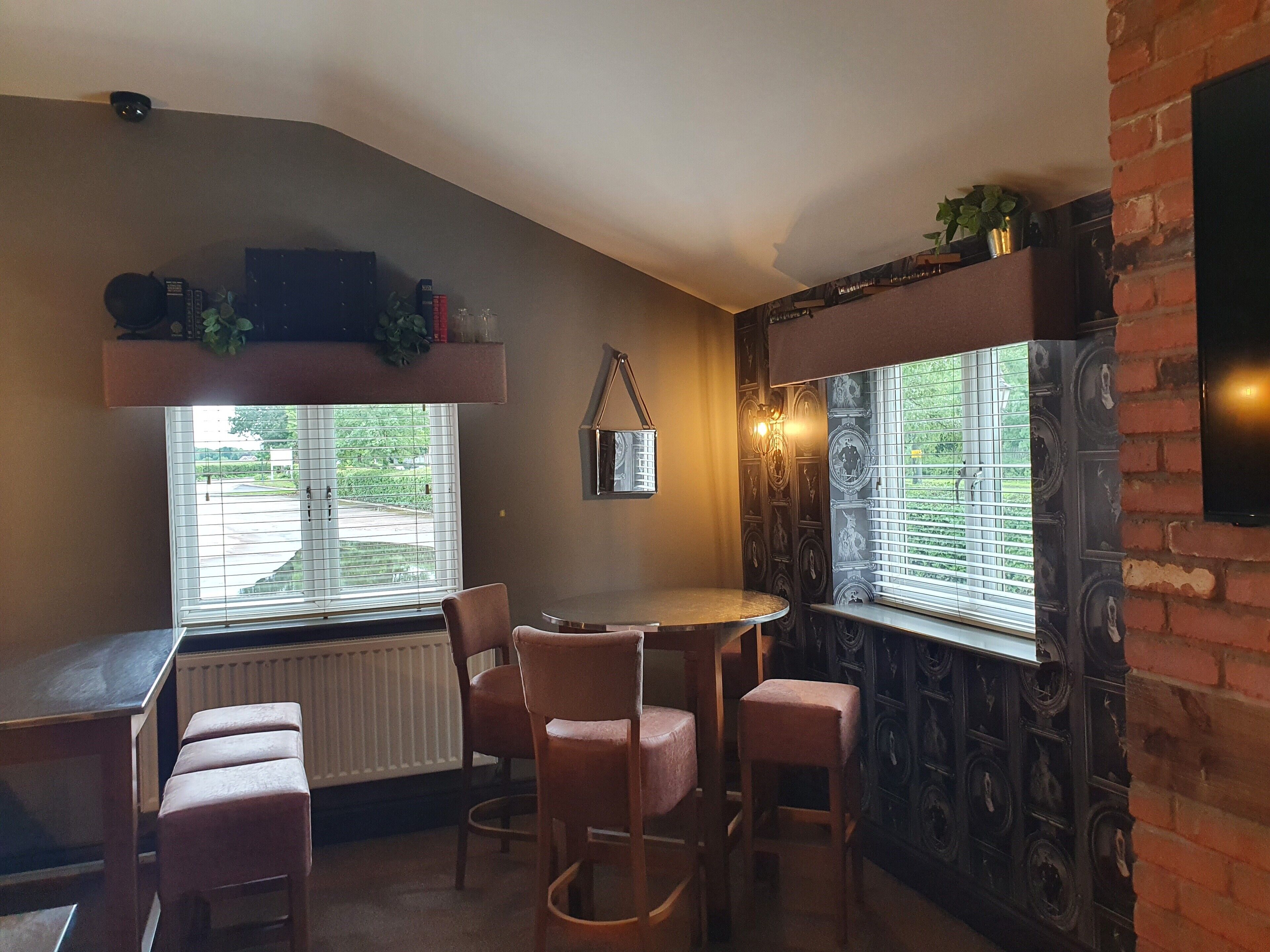 Una habitación acogedora con una mesa redonda y cuatro sillas, un radiador, una ventana con persianas y una pared de ladrillo con detalles decorativos.