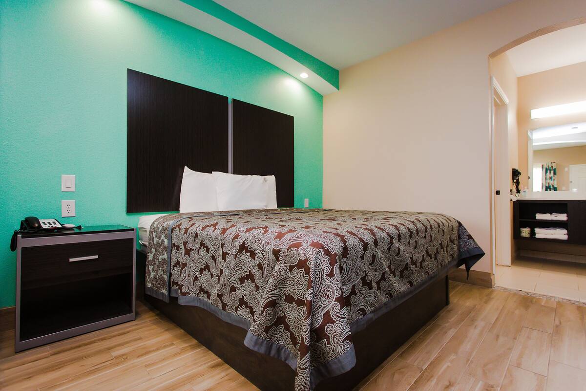 Une chambre d’hôtel avec un lit, une table de chevet, un bureau et une salle de bain visible à travers une porte ouverte.