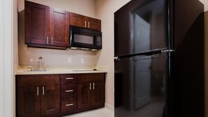 A kitchen with dark wooden cabinets, a stainless steel sink, a black refrigerator, and a microwave above the cabinets. - Palace Inn and Suites - Willowbrook Mall (Houston)